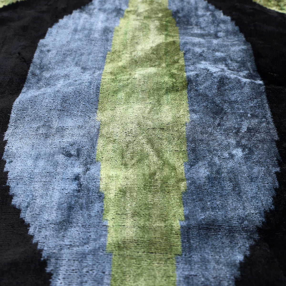 Close-up of olive moss velvet with a central stripe and slate blue stepped ikat pattern