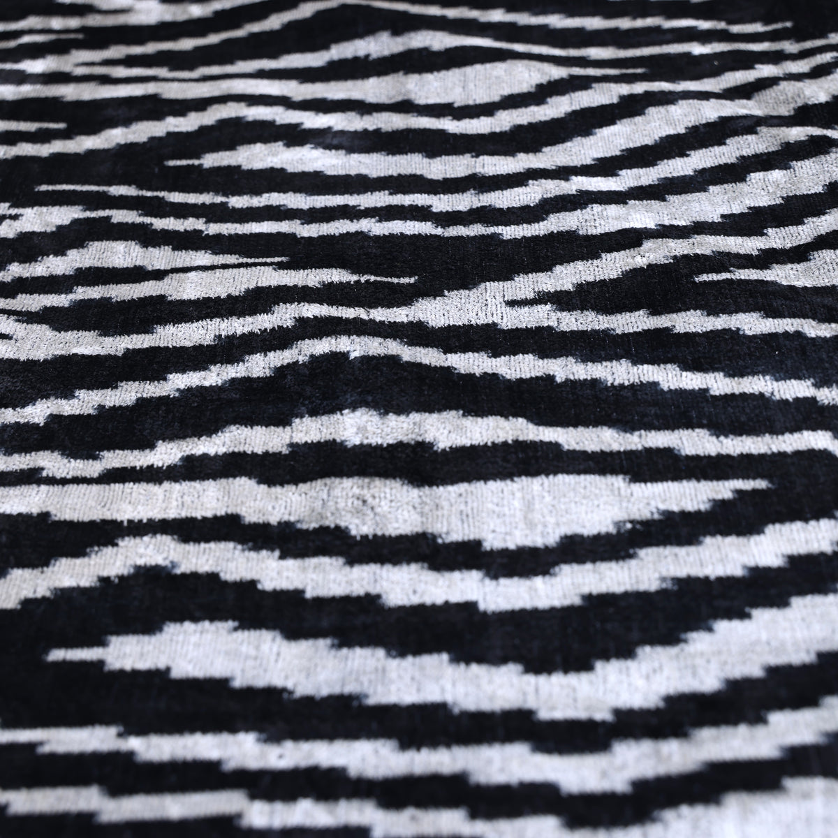 Close-up of inky black and soft ivory ikat stripe silk velvet with zebra-inspired movement