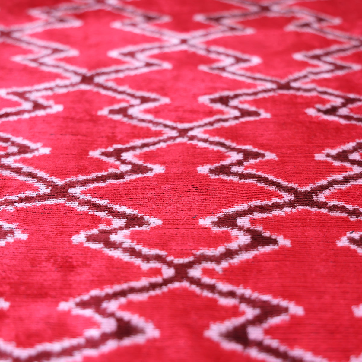 Angled view of cherry red and off-white ikat diamond lattice on velvet