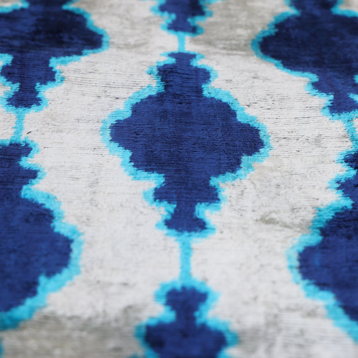 Angled close-up of cobalt royal blue and turquoise ikat medallions on silvery white velvet