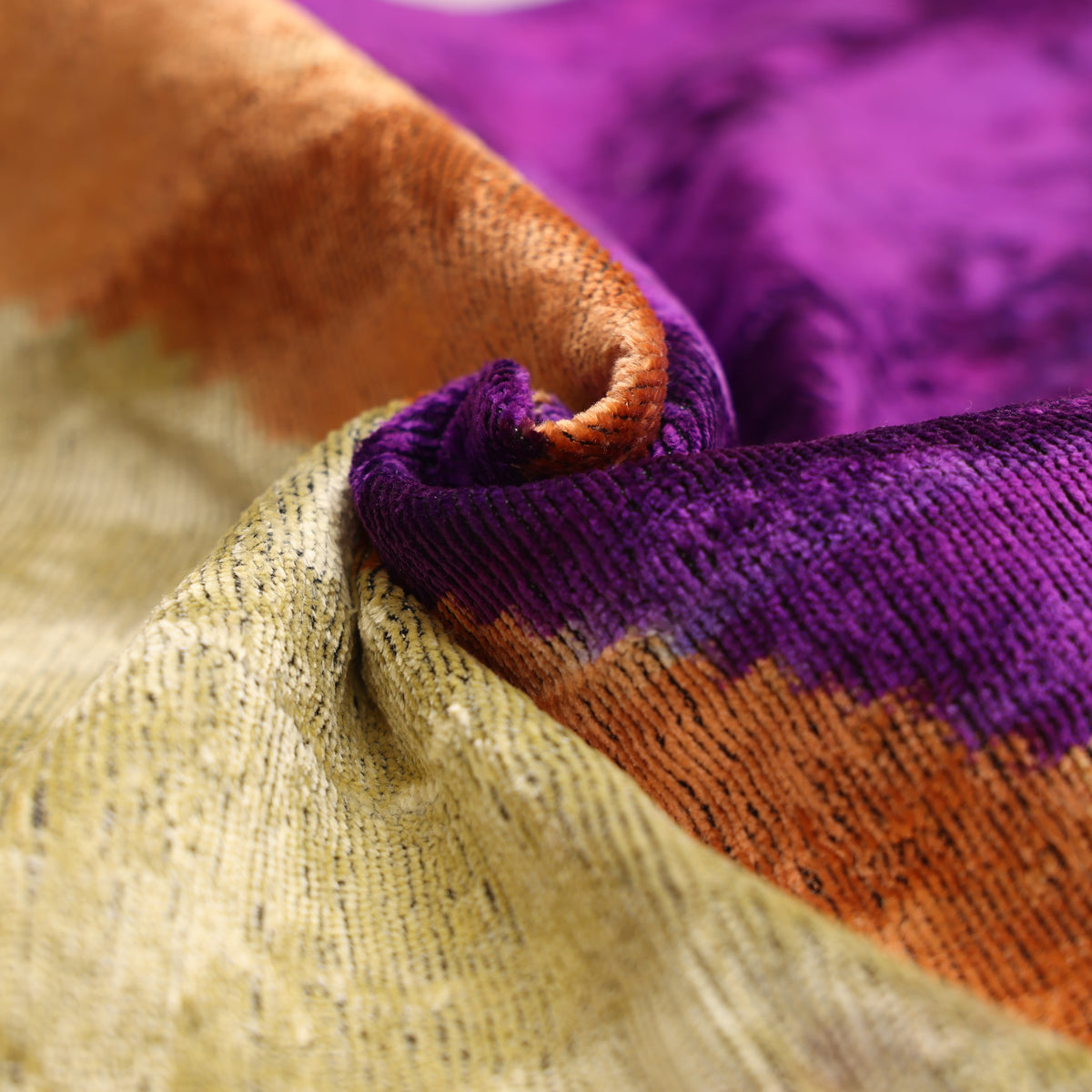 Folded geometric velvet showing ribbed pile texture in purple and champagne gold