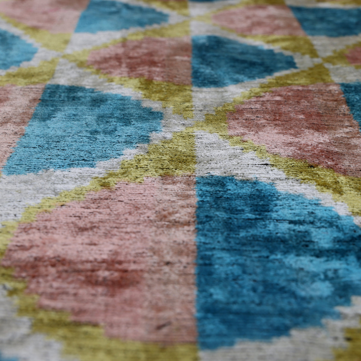Raking light across dusty rose pink and cerulean blue geometric ikat velvet