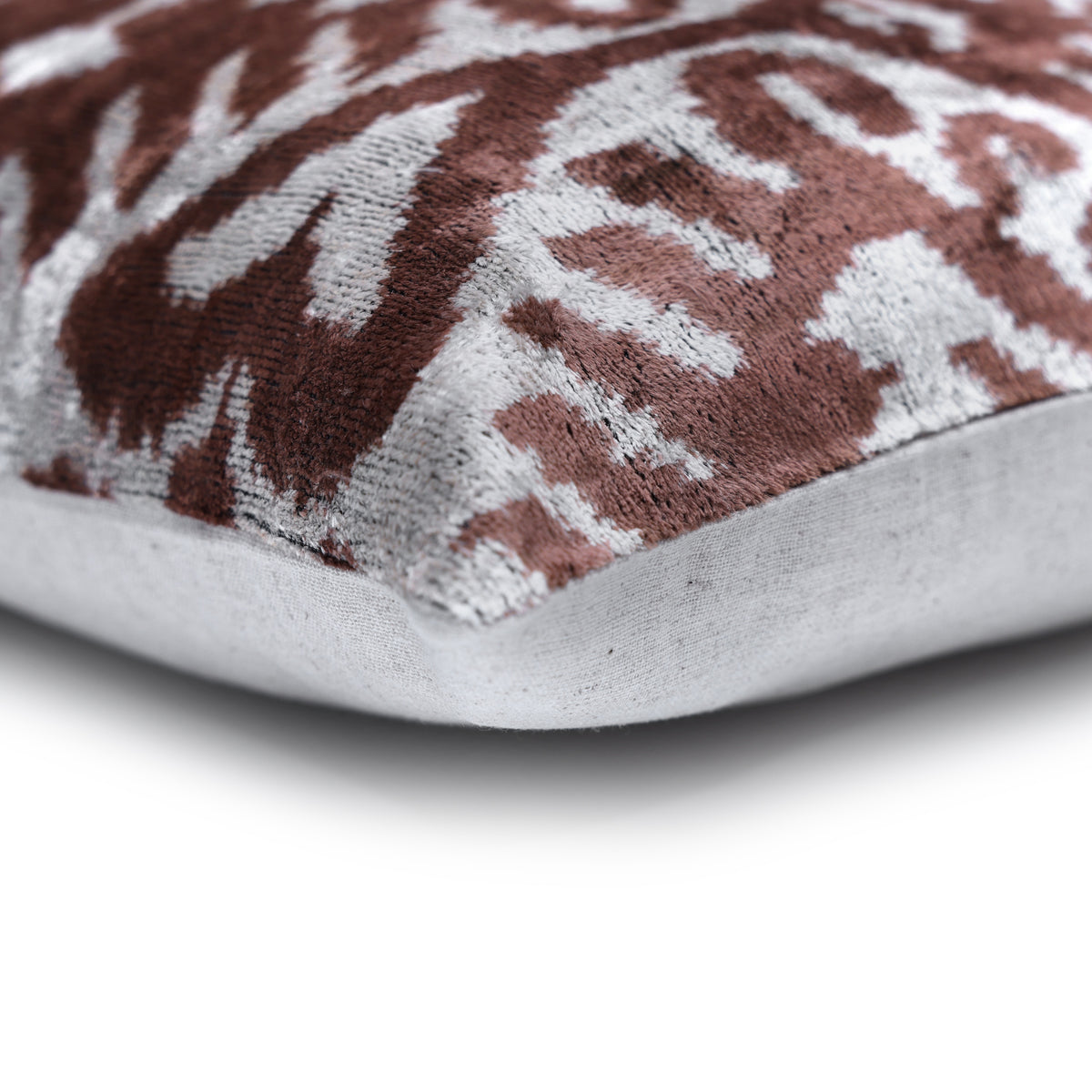 Corner detail of warm brown and silvery white ikat pillow with knife edge and light backing