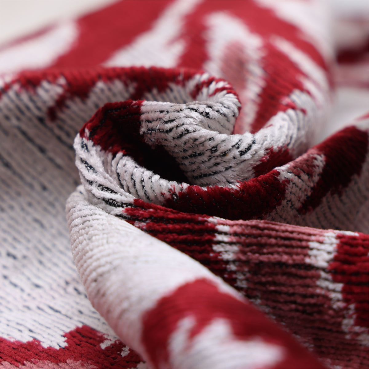 Macro view of folded silk velvet showing ribbed texture in crimson and silvery off-white