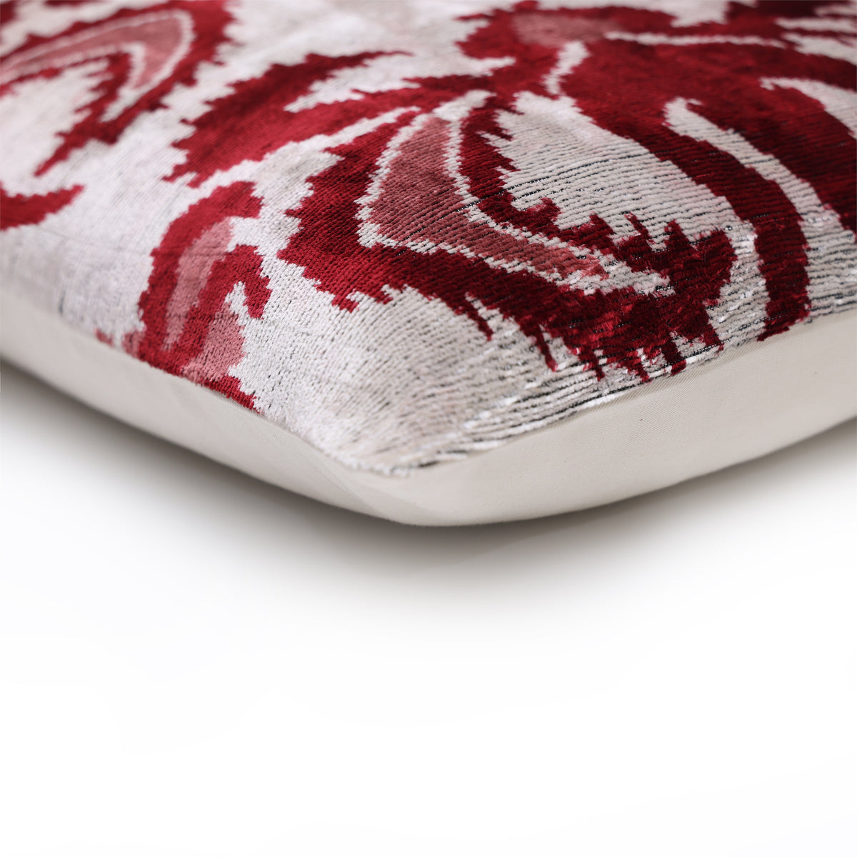 Corner detail of crimson and silvery off-white lumbar pillow with smooth seam and solid backing
