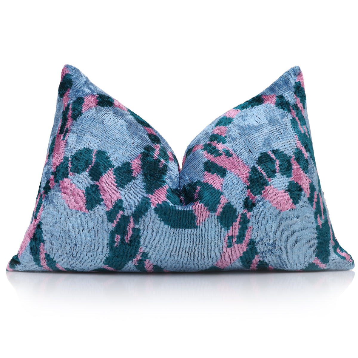 Styled ice blue, dark teal and rose pink ikat lumbar pillow on a reflective surface