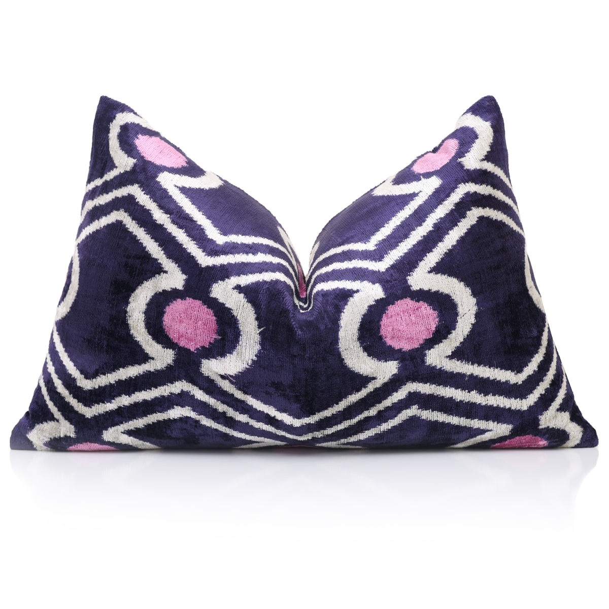 Deep indigo purple and white geometric lumbar pillow with mauve pink accents, karate chop styled on reflective surface