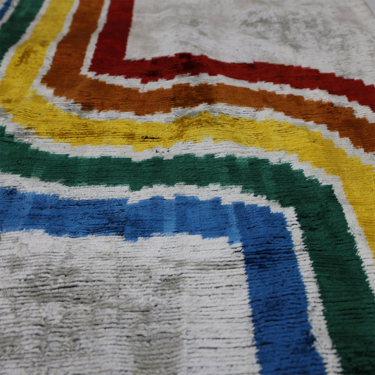 Low-angle view of silvery off-white velvet pile with colorful wave stripe sheen