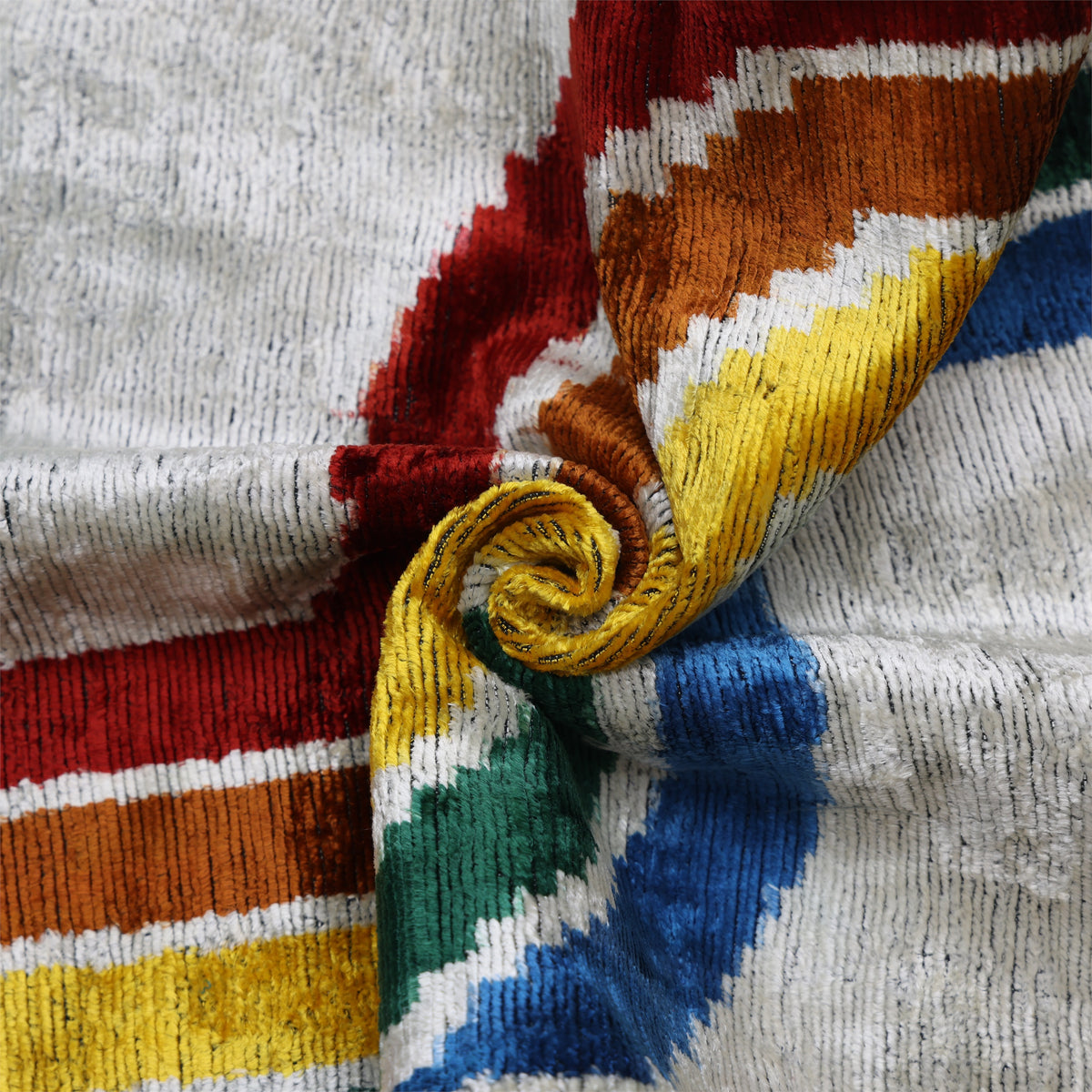 Overhead close-up of cut velvet pile in silvery off-white, gold, emerald and crimson waves