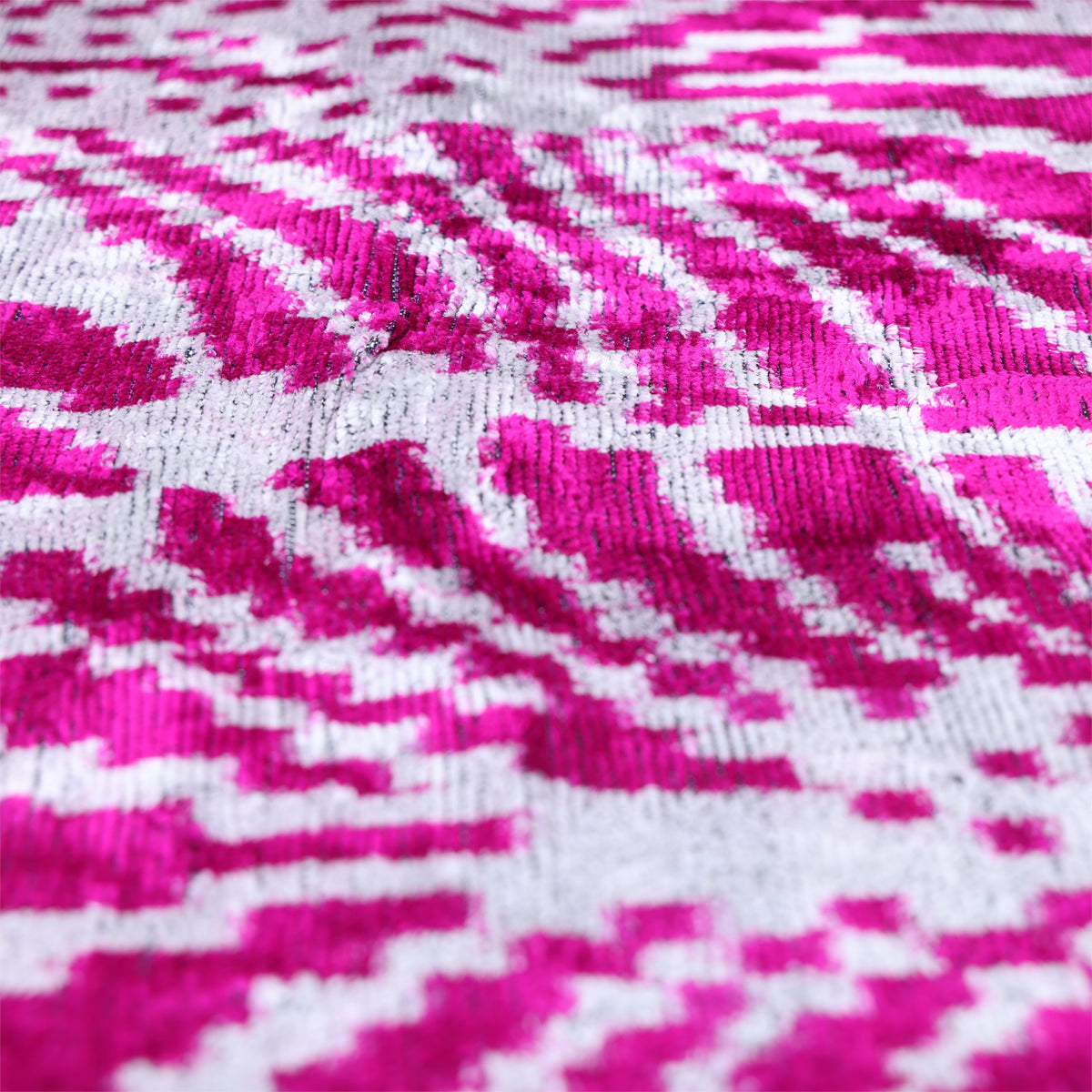 Angled close-up of magenta pink and crisp white ikat pattern with visible velvet sheen