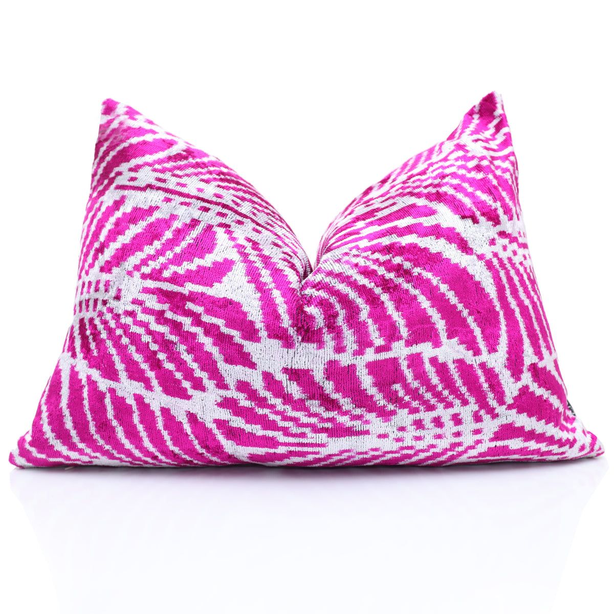 Magenta pink and crisp white ikat lumbar pillow styled with a center chop on a reflective white surface
