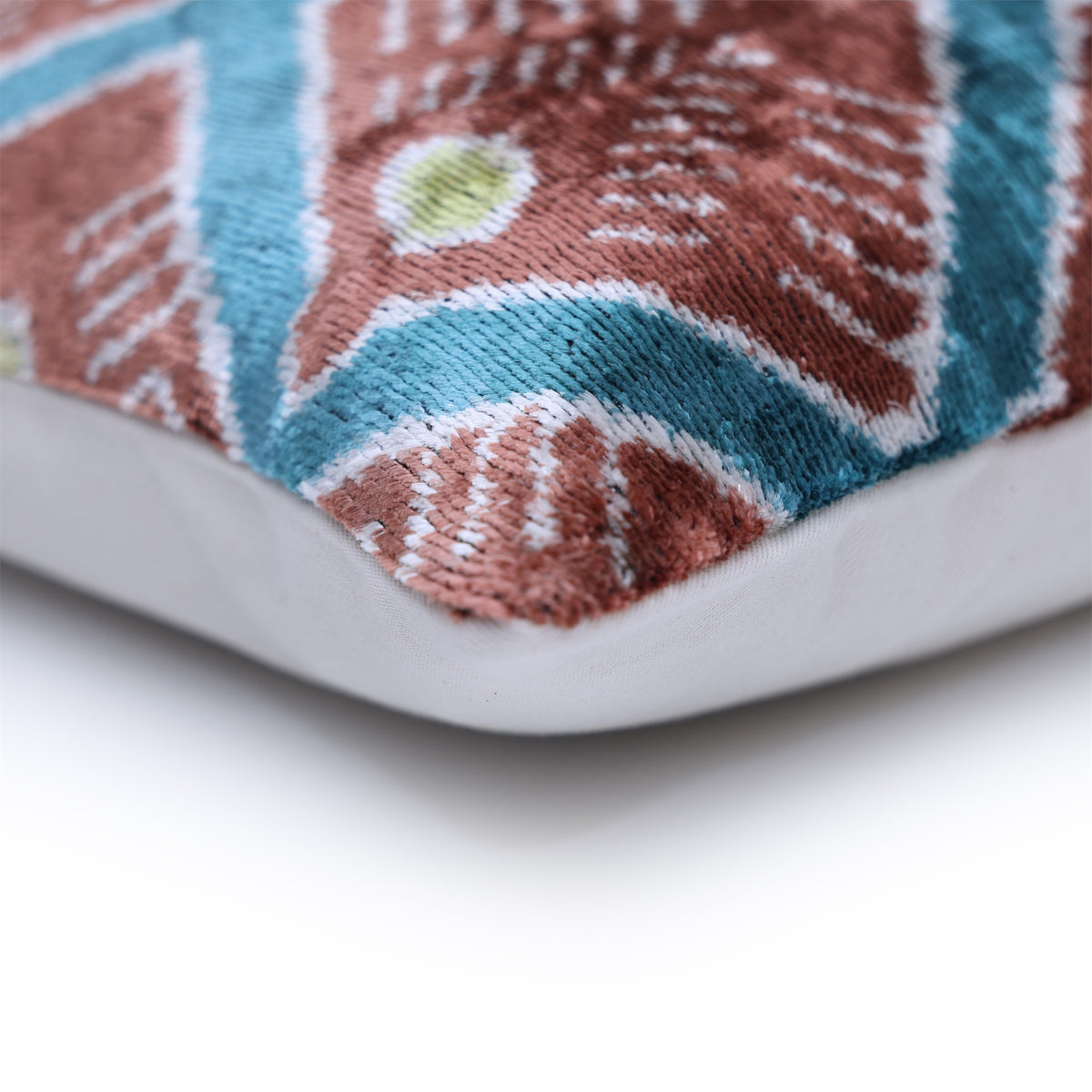 Corner seam of geometric velvet pillow showing terracotta rust pile and teal pattern
