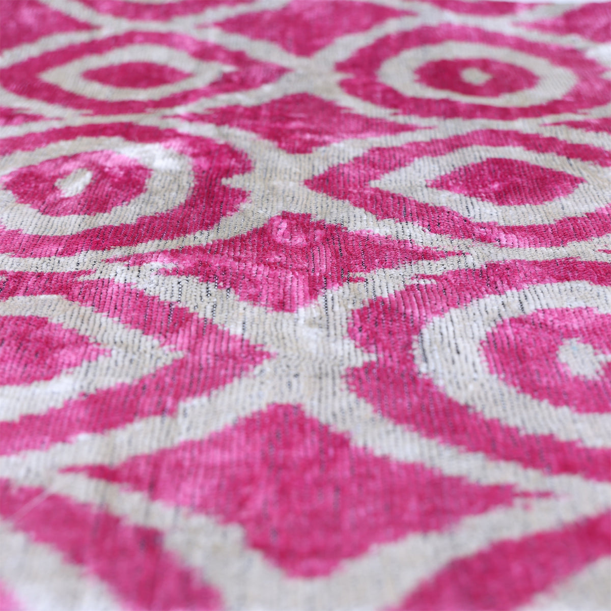 Angled view of fuchsia pink and silvery white geometric ikat velvet with visible sheen