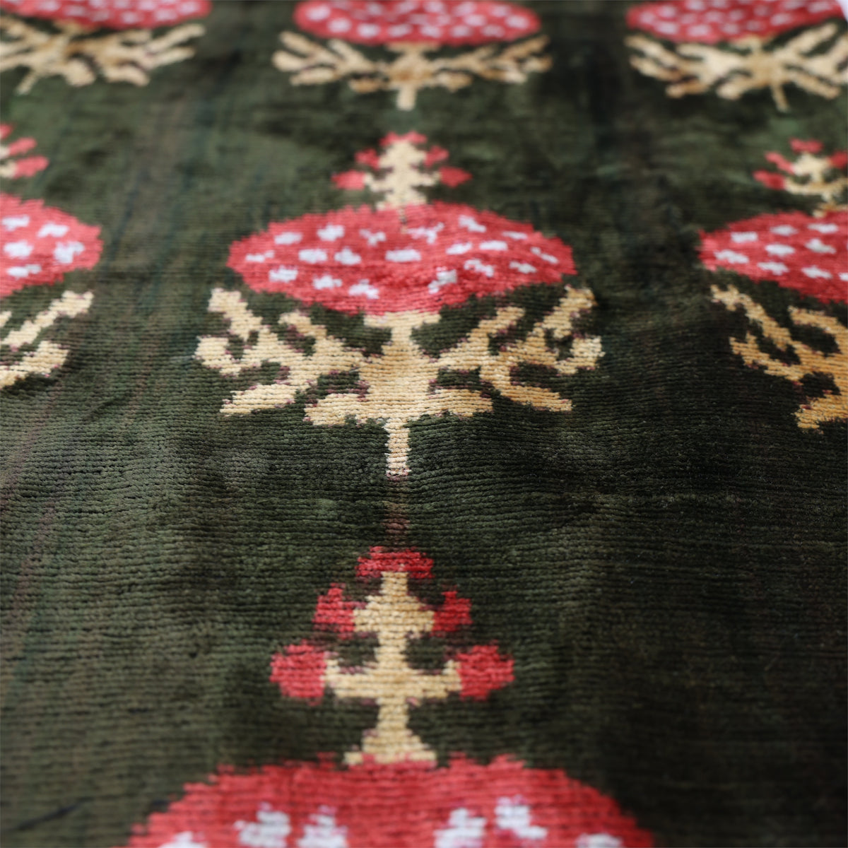 Angled view showing soft sheen, velvet pile and dark olive green botanical ikat pattern