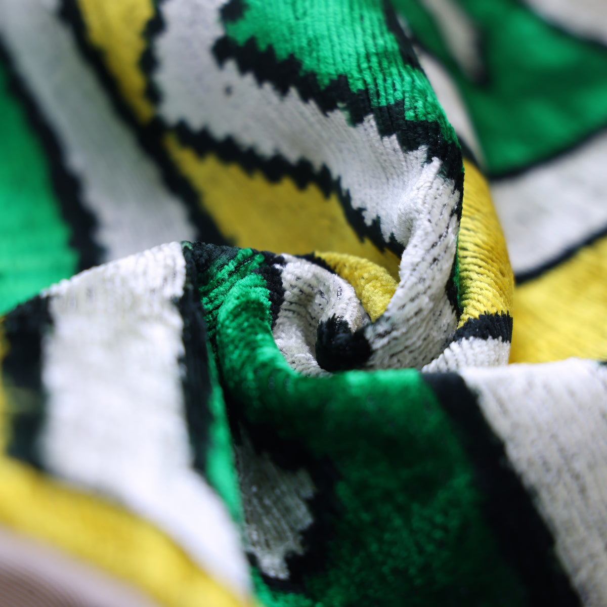 Extreme close-up of folded geometric velvet showing a dense pile and shifting emerald teal sheen