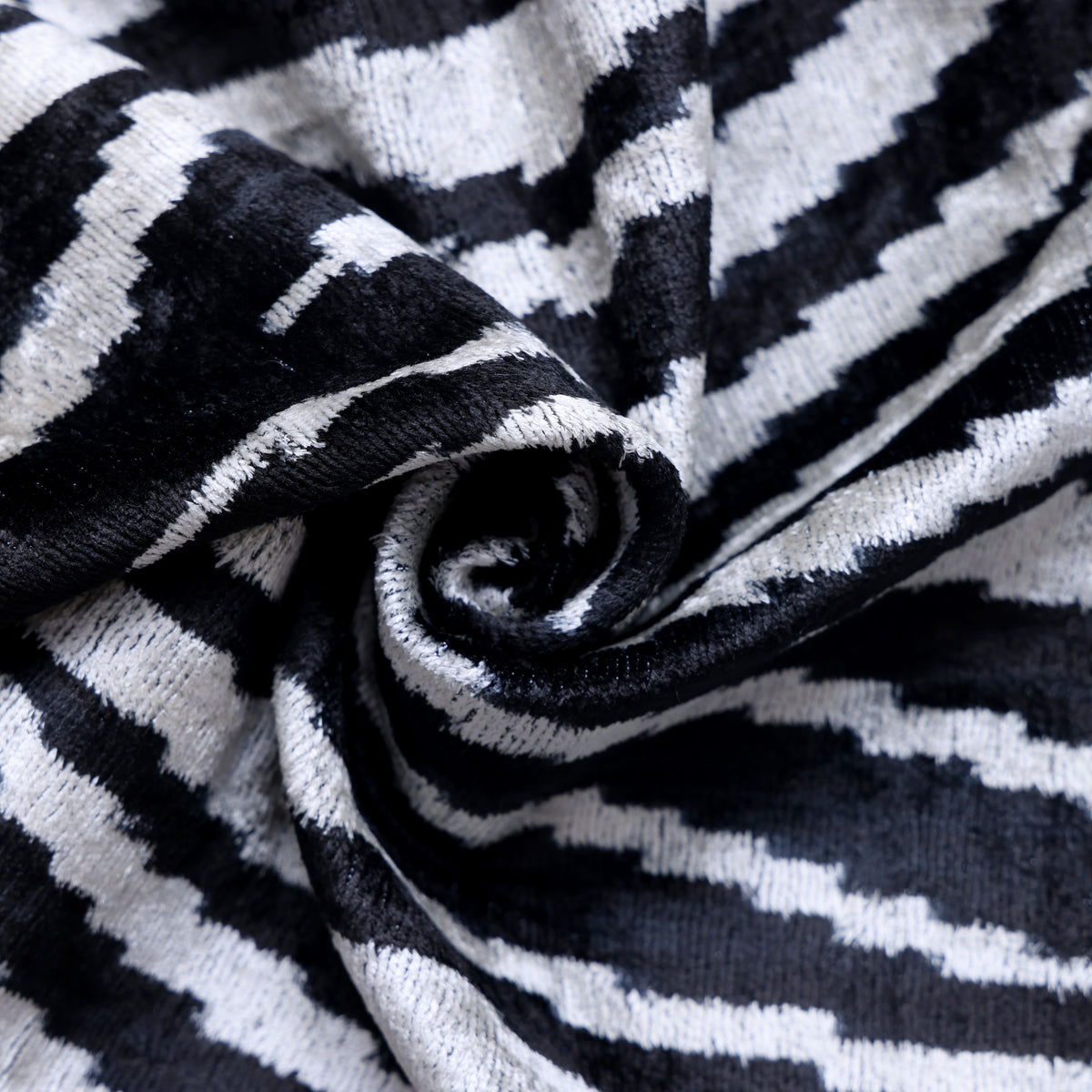 Overhead view of a rolled inky black and soft ivory ikat stripe textile