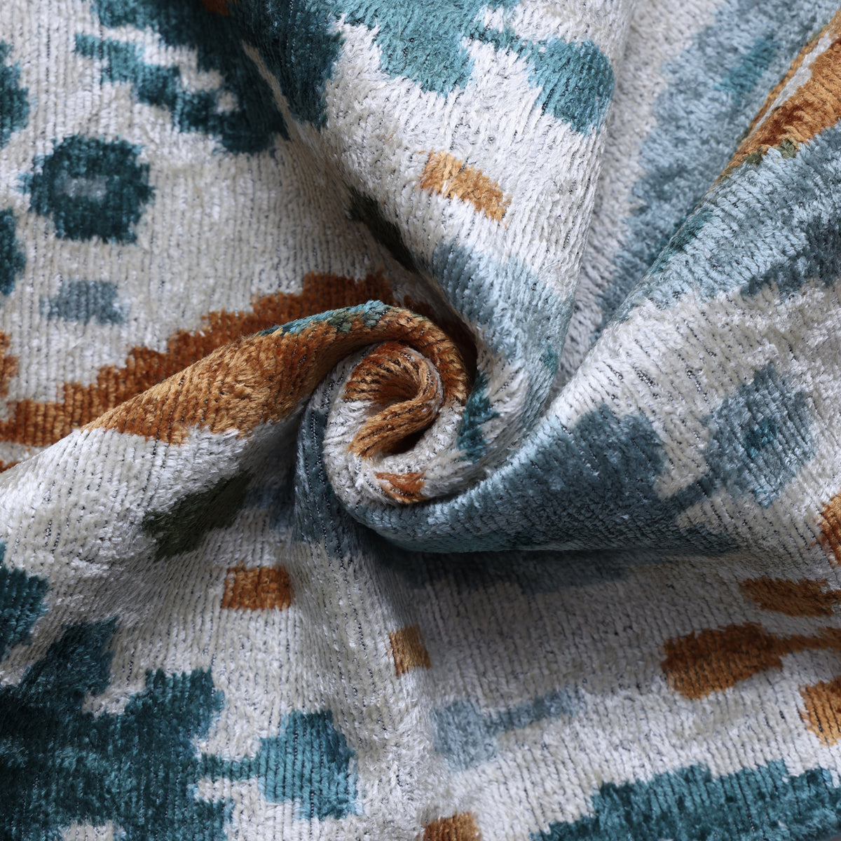 Close view of muted teal blue and ochre gold ikat pattern on plush silk velvet