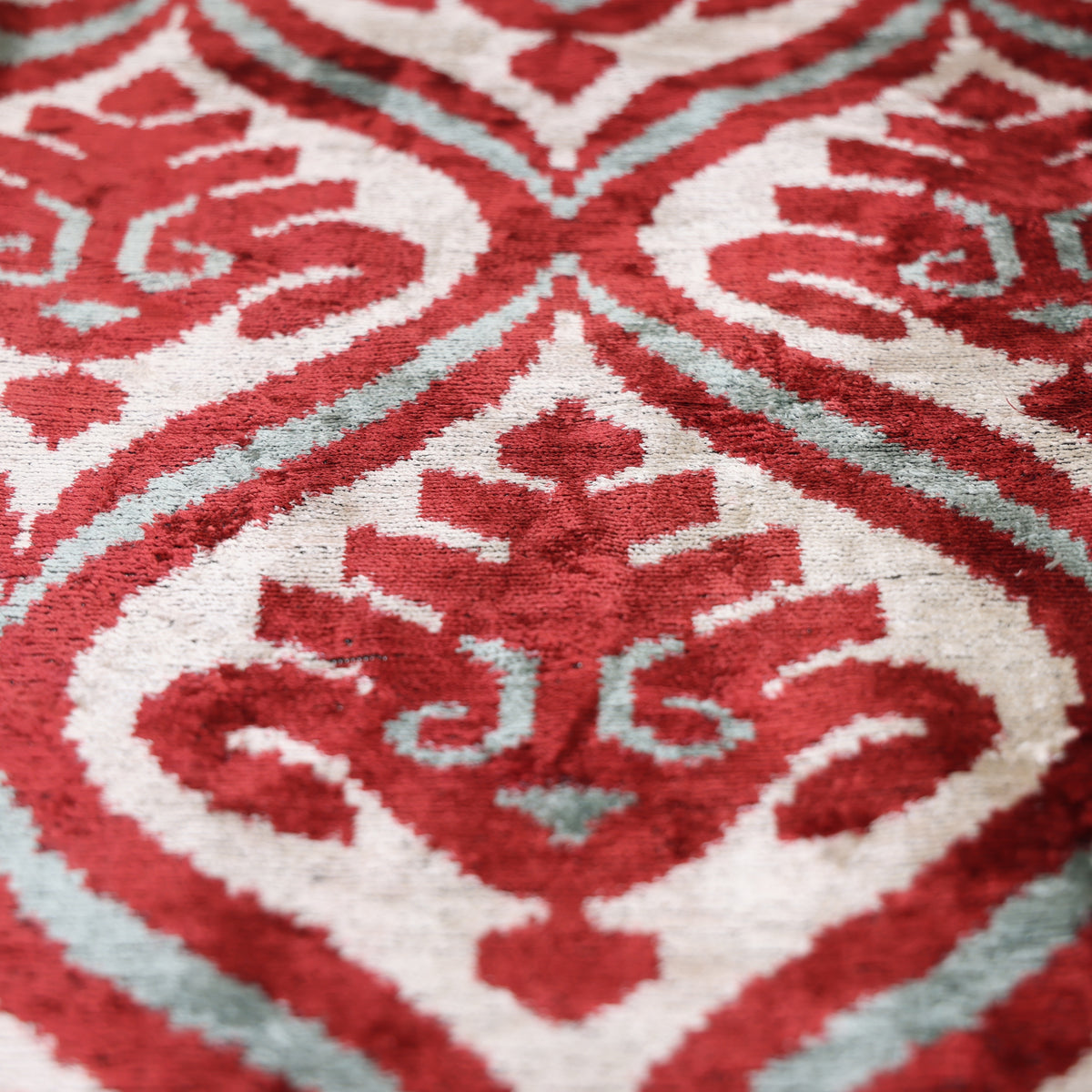 Angled detail of the geometric diamond medallion ikat pattern in crimson and ivory