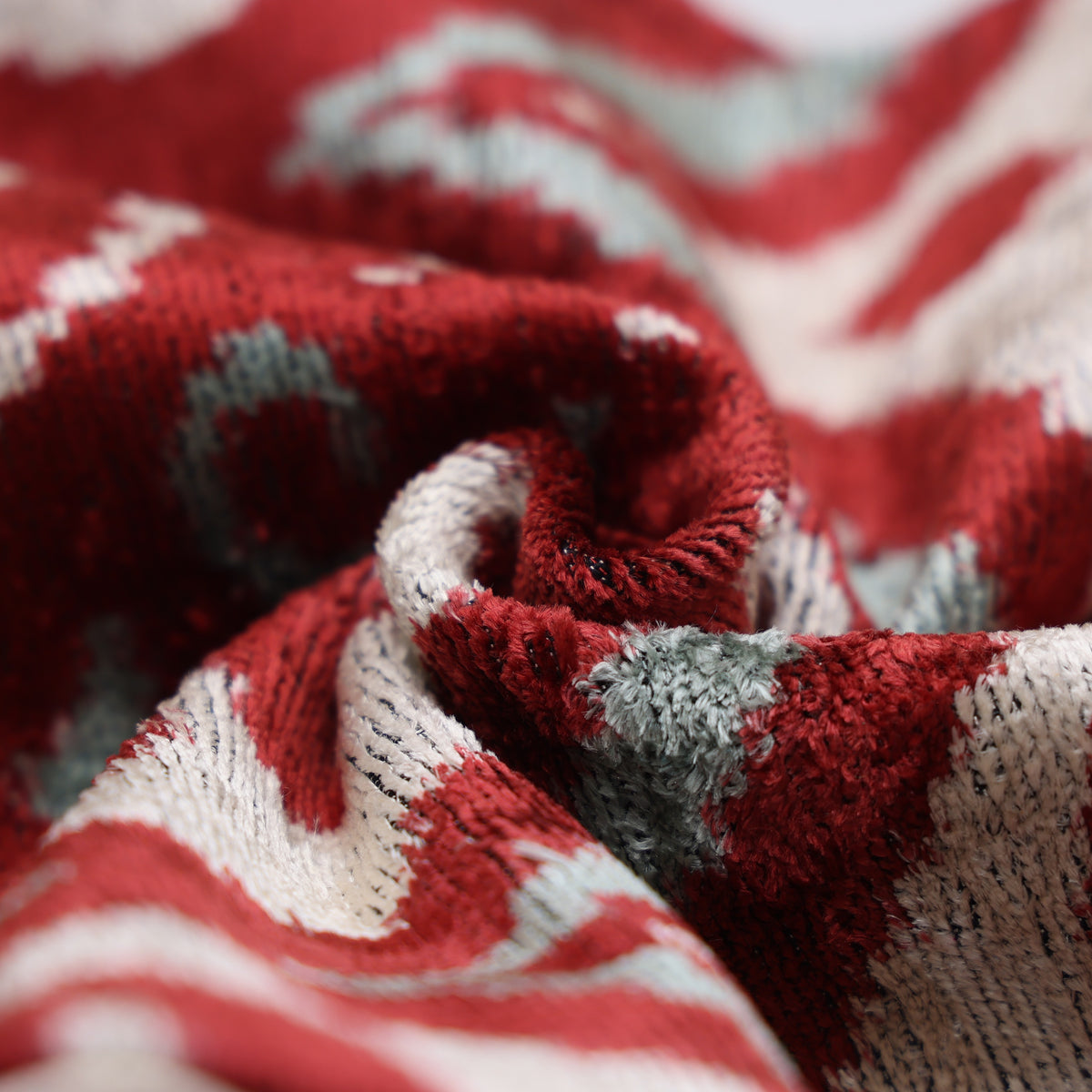 Macro view of swirling crimson red, warm ivory and pale sage aqua velvet