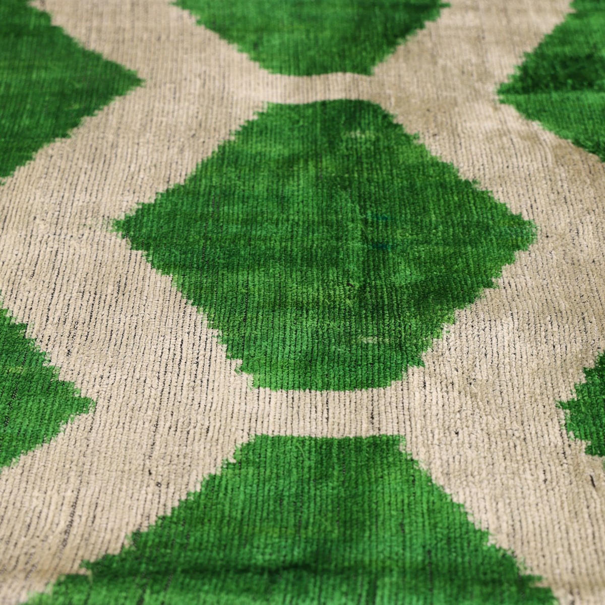 Angled macro view of emerald green and pale greige honeycomb ikat pattern and flat velvet pile