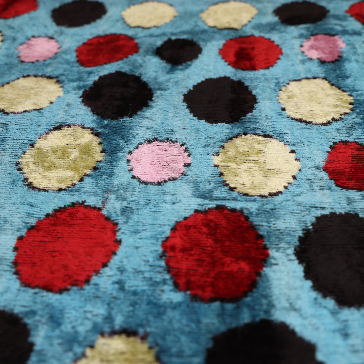 Angled close-up across cerulean blue polka dot velvet showing black and crimson red spots