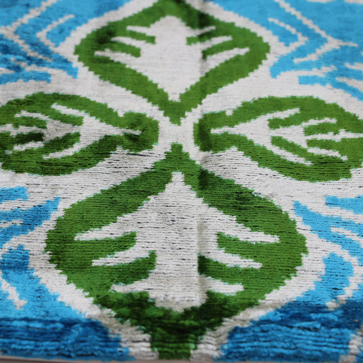 Central bright olive green and soft white four-leaf ikat motif on cerulean teal