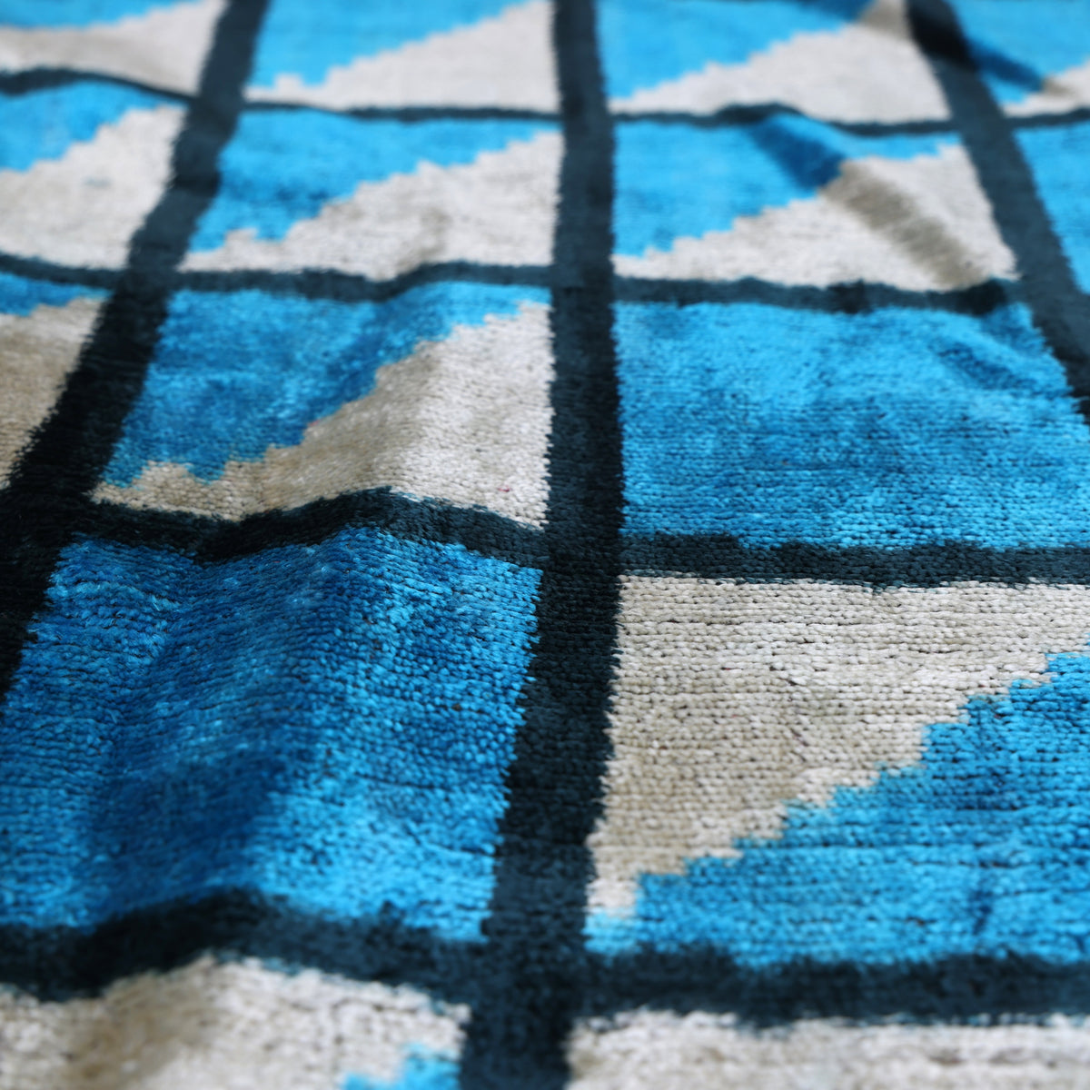 Low-angle view of cerulean blue velvet pile and diagonal triangle grid pattern