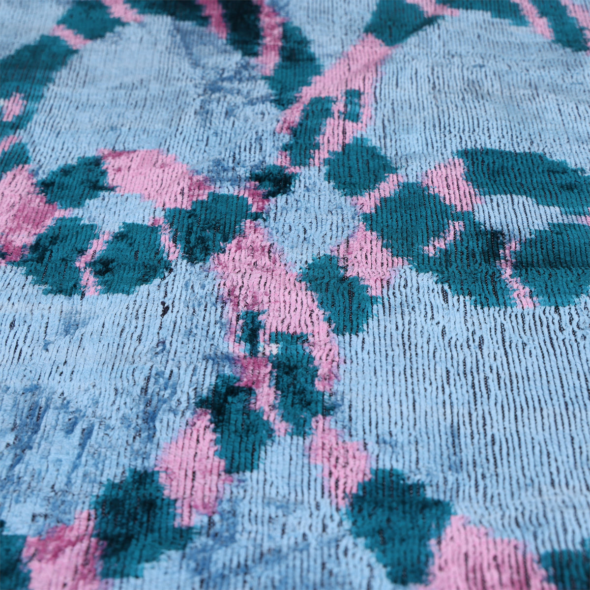 Macro view of dark teal and rose pink woven ikat pattern on ice blue velvet