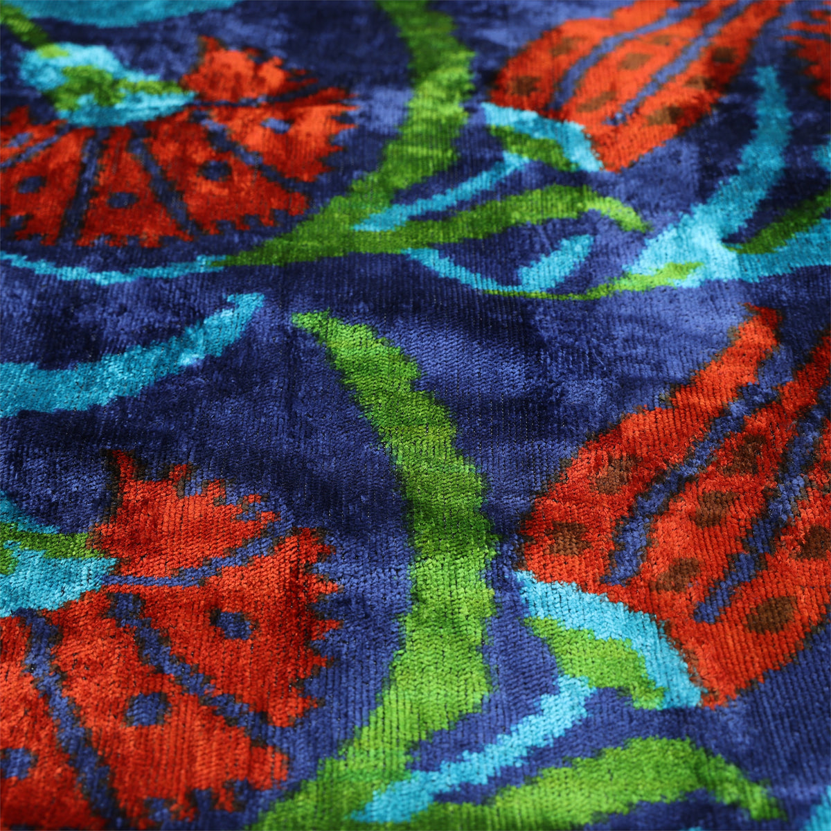 Angled close-up of Ottoman floral velvet surface in deep royal blue, brick red-orange, apple green and turquoise
