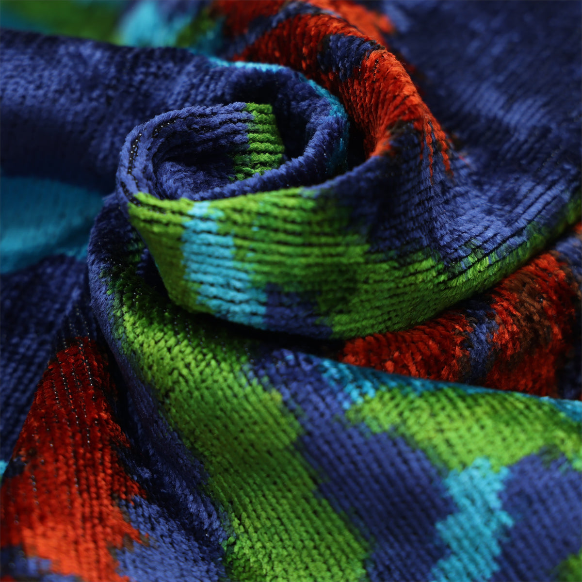 Swirled close-up of deep royal blue silk velvet showing plush pile, weave and jewel-toned floral colors