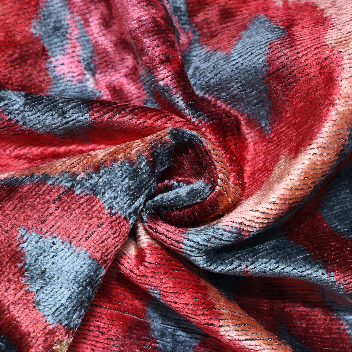 Close-up of crimson red and slate blue-gray cut-velvet ikat fabric with visible sheen