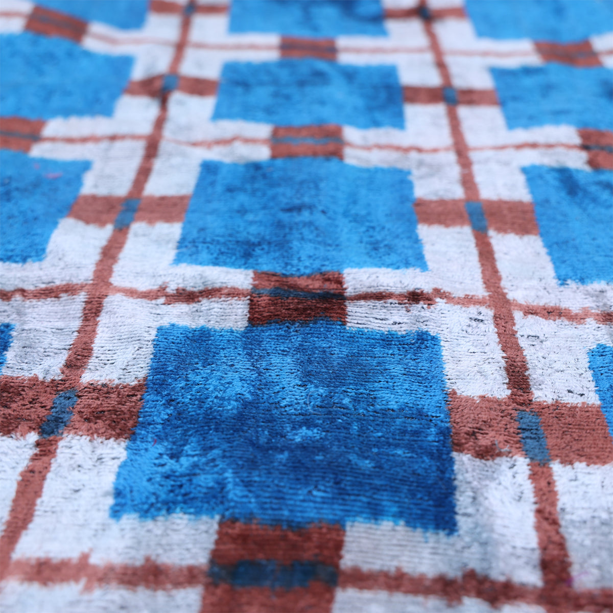 Raking view of bright cobalt blue plaid silk velvet with cool silvery white and reddish brown lines