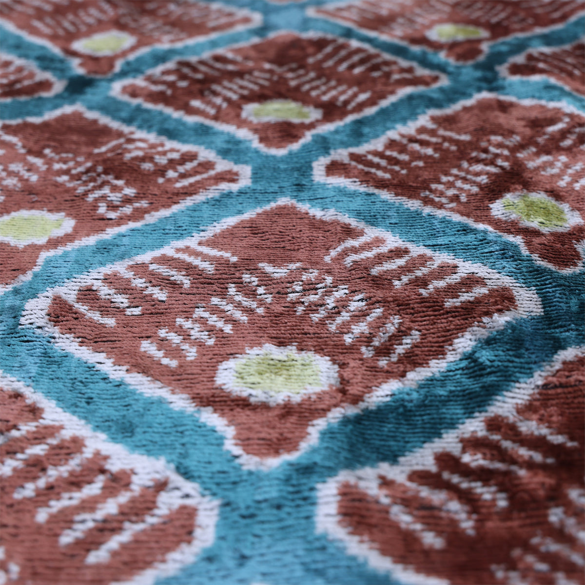 Angled view of geometric diamond ikat pattern in terracotta rust, teal blue and soft white