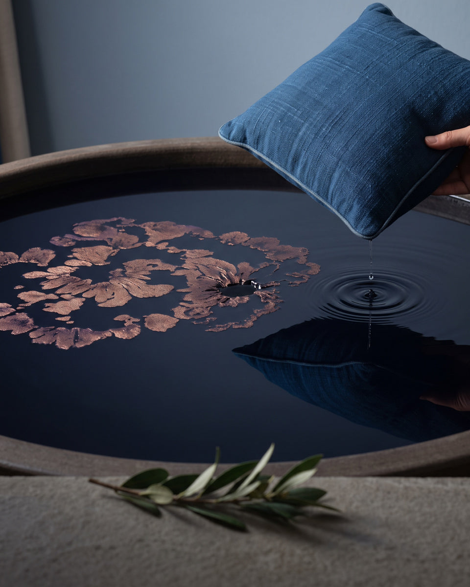 A blue pillow lifted from a dark dye basin, drops rippling the surface