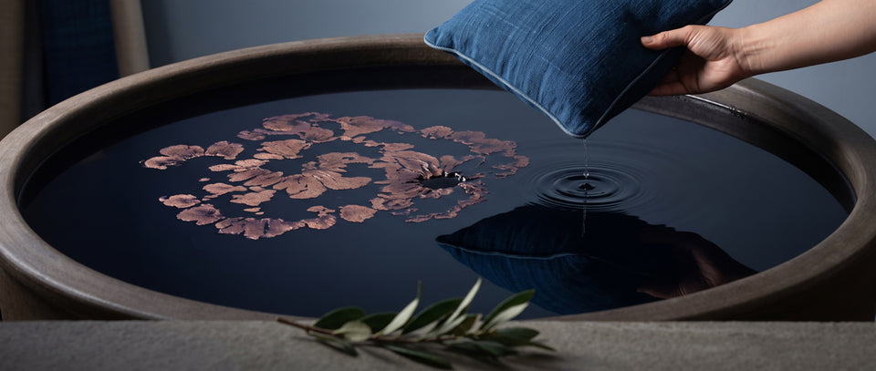 A blue pillow lifted from a dark dye basin, drops rippling the surface