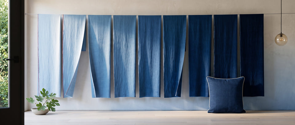 Lengths of cloth hung in a row from pale to deep indigo, a navy pillow in front