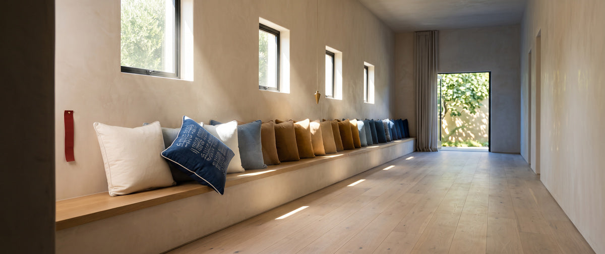 A long hall with a built-in bench lined with pillows in bone, ochre and blue