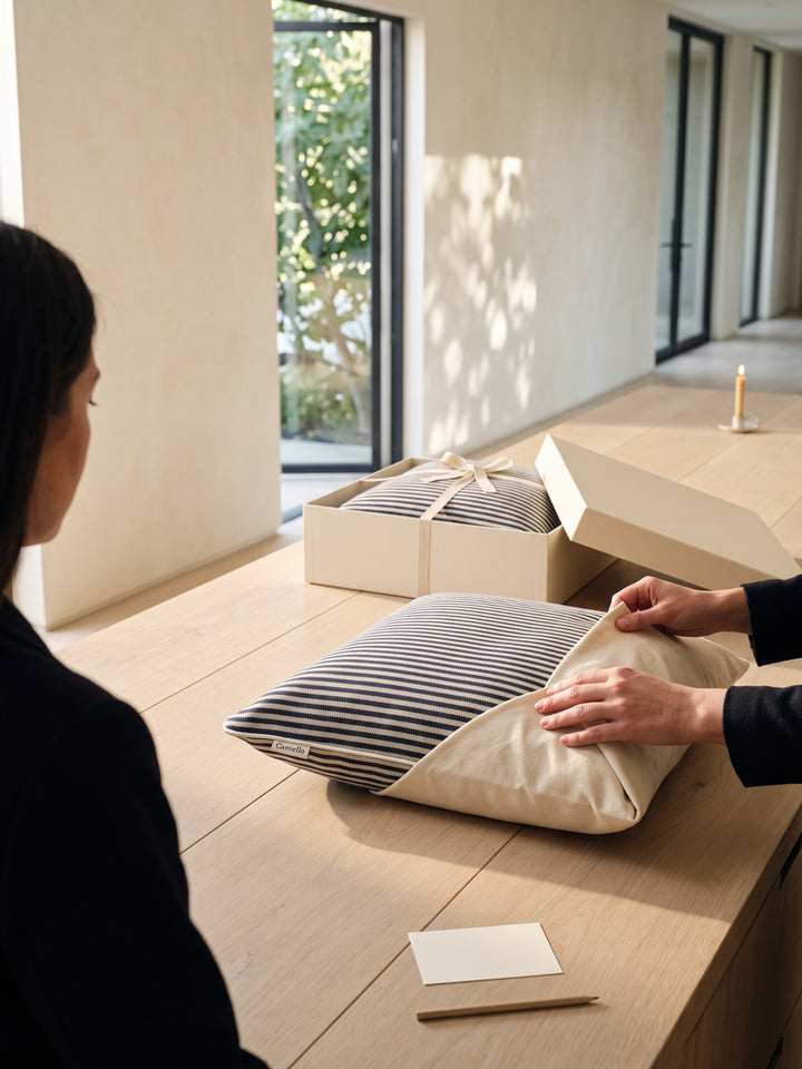 Hands wrapping a striped pillow in cotton at a long packing table